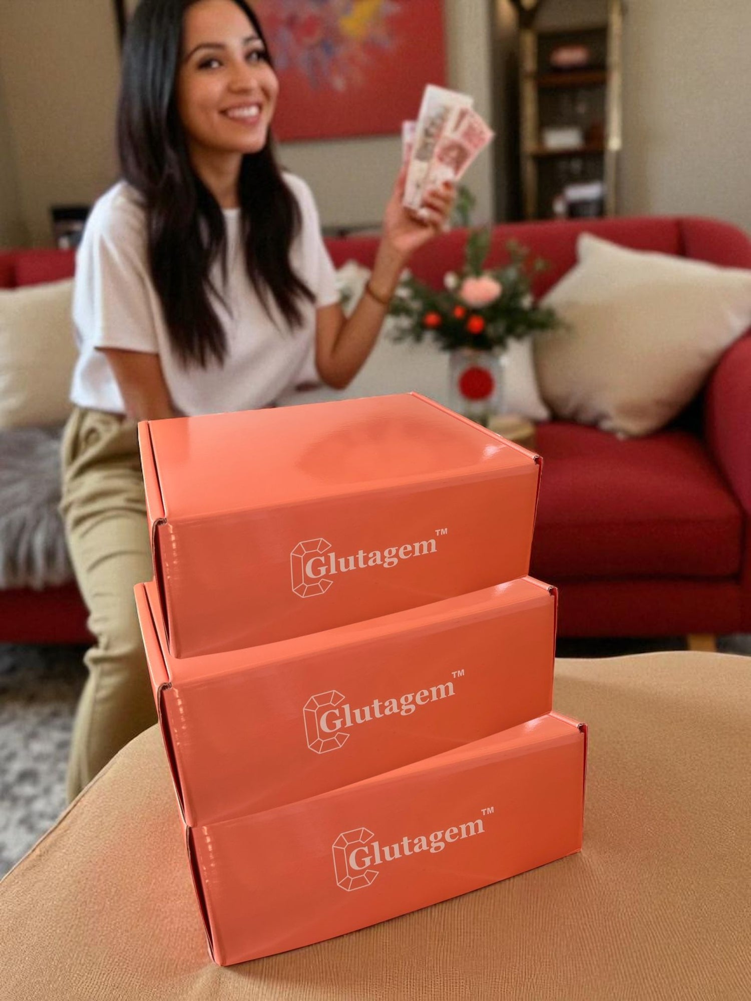 Woman holding her commission cash next to stacked Glutagen boxes in a living room setting.