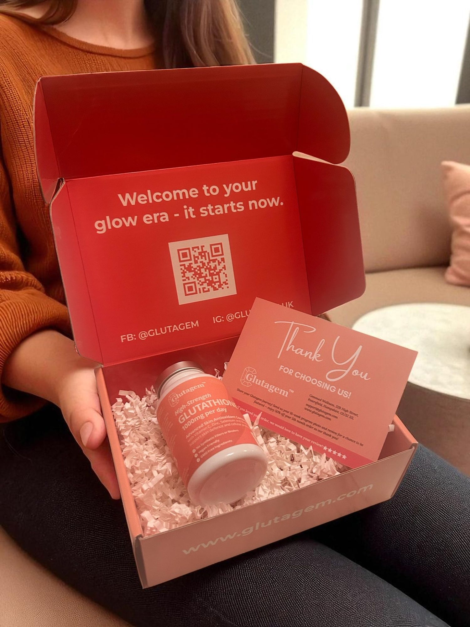 Woman holding a red and pink Glutagem product box with a Glutagem Glutathione tub and thank-you card inside, featuring Glutagem branding.
